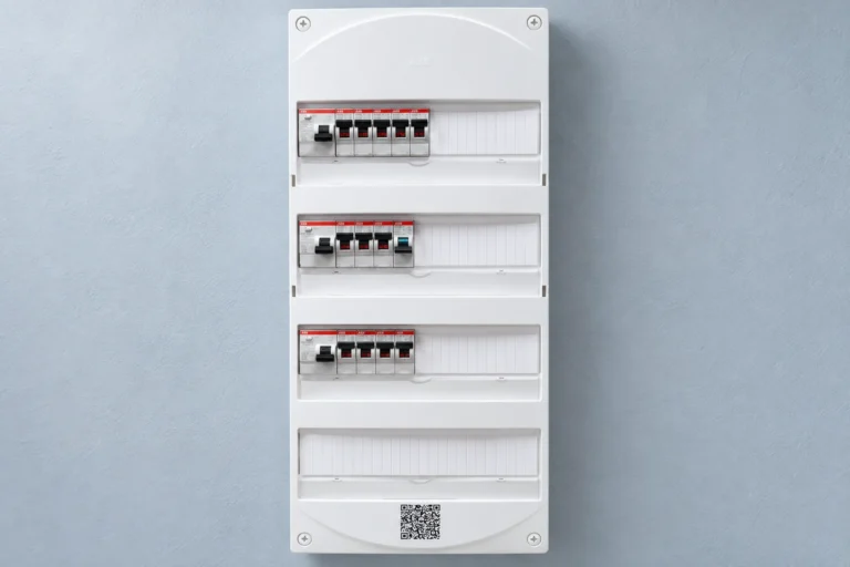 Tableau électrique blanc à quatre rangées, avec des appareils modulaires et des emplacements libres, sur un mur clair.